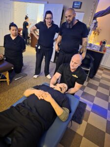 Massage therapy instructor at Texas Massage Academy guiding students through neck massage techniques during an in-person class.