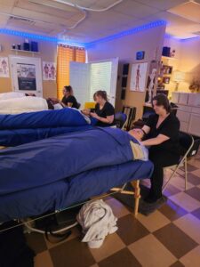 Massage therapy students at Texas Massage Academy practicing hands-on techniques in a classroom with blue treatment tables and instructors observing.